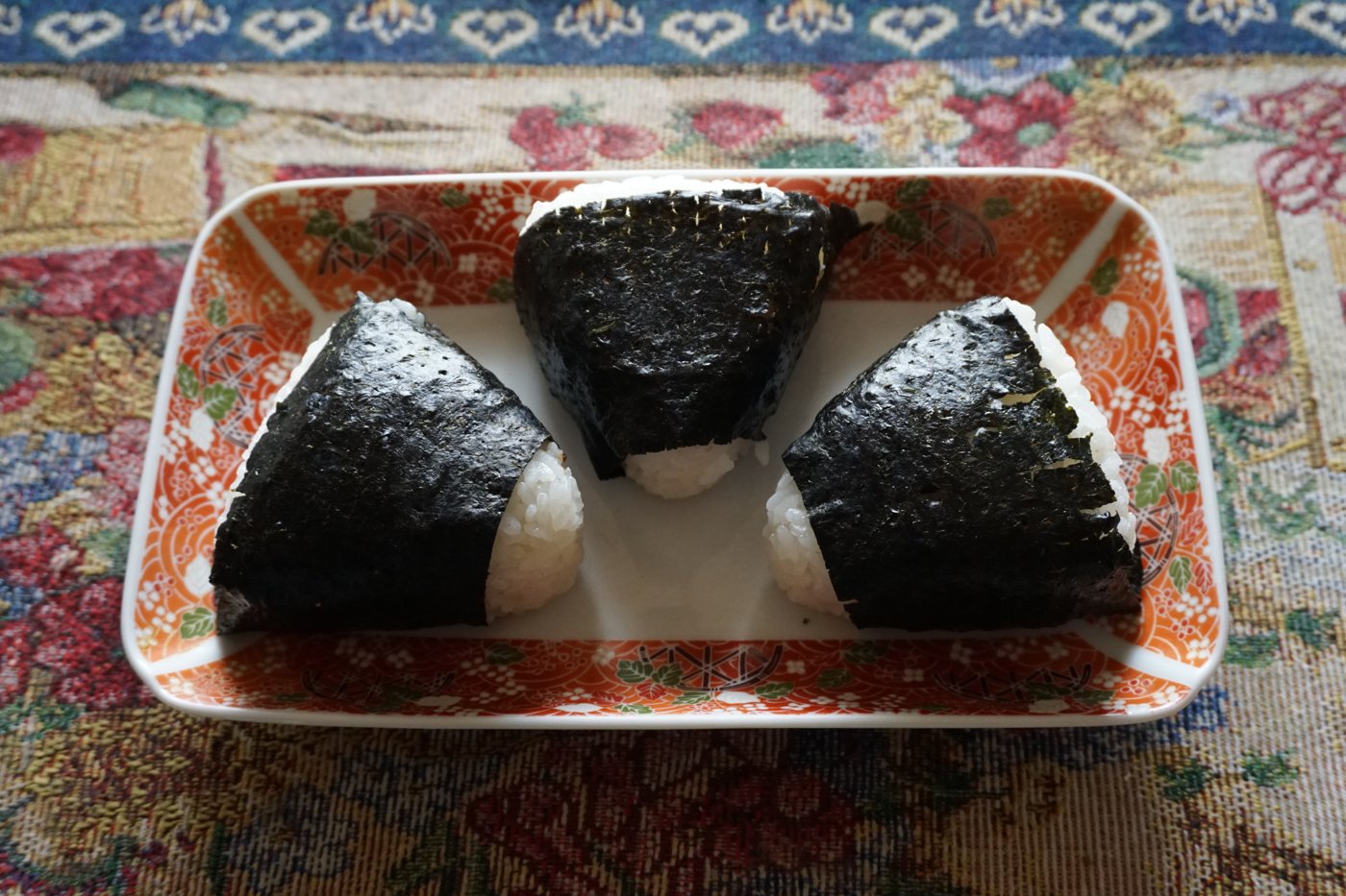 和皿に並んだ三角むすび。海苔と塩と、握った手のあとがあれば、それだけでごちそうだった。(Photo: 些細な日常 / CC BY-SA 4.0, via Wikimedia Commons)